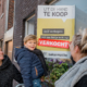 Mama met kind die verkocht-sticker plakt op vastgoedbord